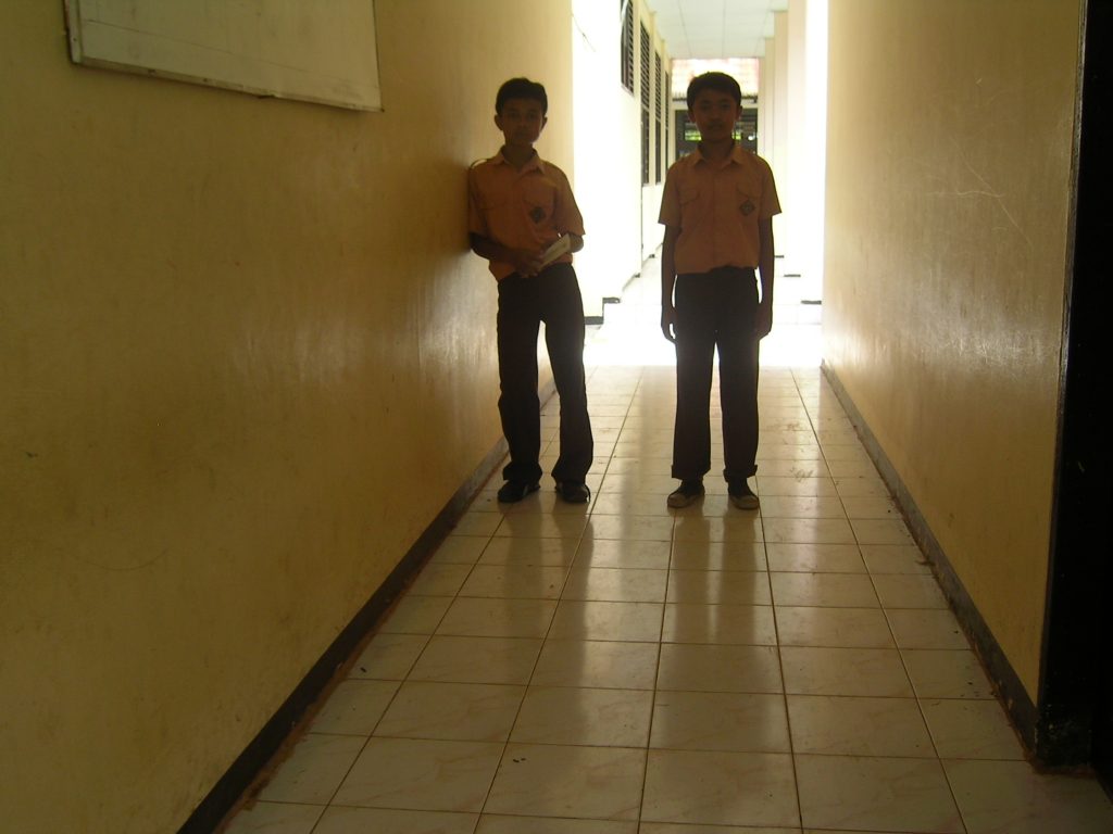 Two boys stand in a dark, narrow corridor. One is leaning on the wall